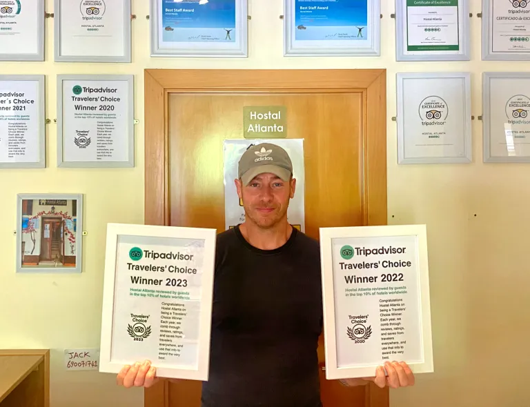 A member of the Atlanta team standing in reception, holding two Tripadvisor Travelers' Choice award certificates, with a wall of framed awards behind